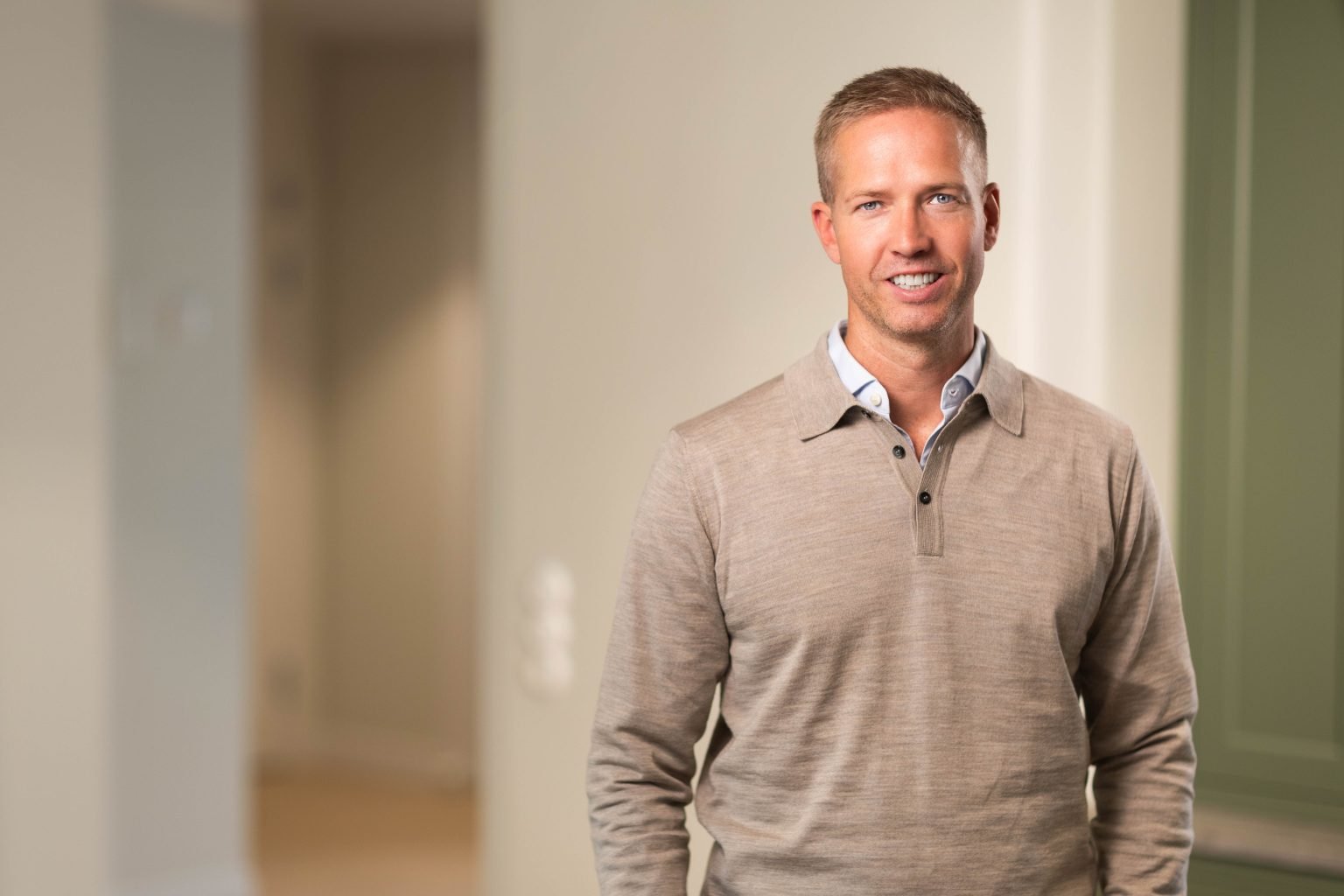 Man in beige sweater standing indoors.