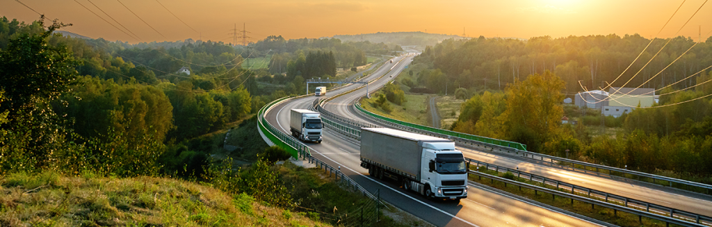 Trucks driving on a highway surrounded by greenery.