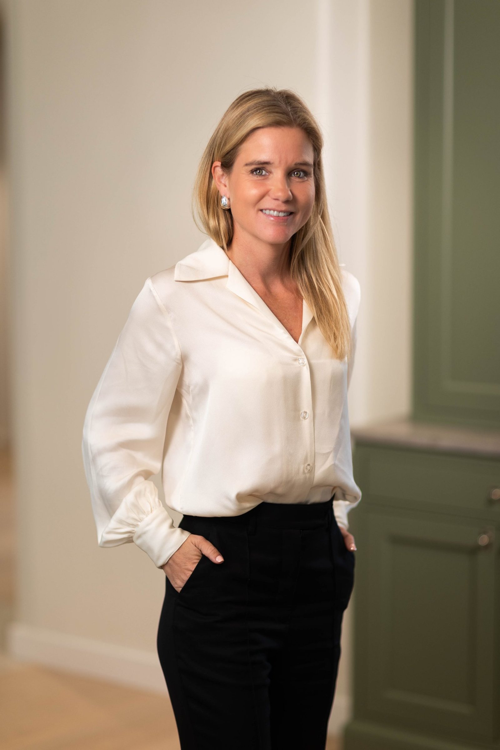 Woman in white blouse and black pants smiling indoors.